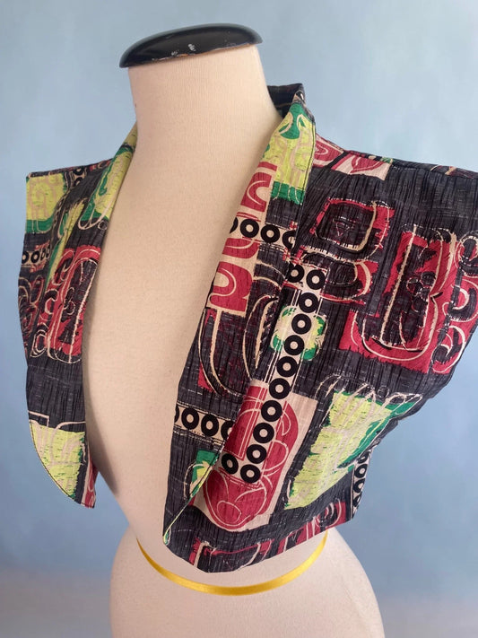 Vintage-inspired cropped top with bold abstract print in red, green, black, and yellow on mannequin