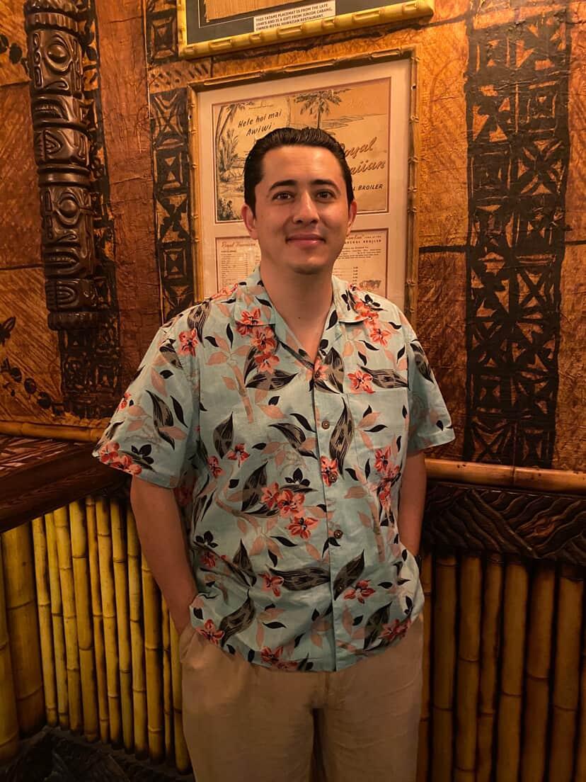 Man wearing vintage-inspired Hawaiian shirt with floral print, standing in tiki-themed setting